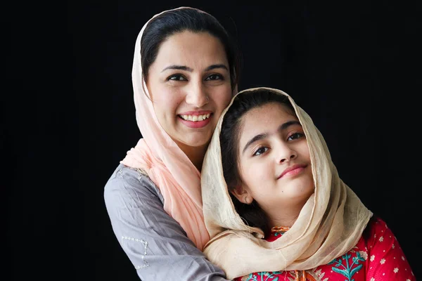 可愛いです笑顔の肖像パキスタンのイスラム教徒の女の子で美しい目と彼女の母親身に着けていますヒジャーブ伝統的なドレスで暗い黒の背景 暖かい愛で幸せなイスラム教徒の家族の母と娘 — ストック写真