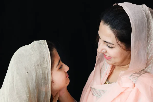 愛らしい笑顔パキスタンのイスラム教徒の少女と美しい目は彼女の母親を見て 女性は黒の背景に伝統的なドレスでヒジャーブを身に着けています 幸せなイスラム教徒の母親と娘の家族の暖かい愛 — ストック写真