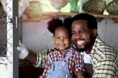 Mutlu çiftçi ailesi sığırlarda birlikte çalışır, gülümseyen Afrikalı baba ve siyah kıvırcık saçlı kız kız tavuk kümesinde tavuk yetiştirir, çocuk ve hediyeler çiftlikte tavuk beslemenin keyfini çıkarırlar..