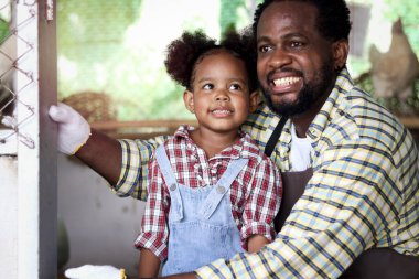 Mutlu çiftçi ailesi sığırlarda birlikte çalışır, gülümseyen Afrikalı baba ve siyah kıvırcık saçlı kız kız tavuk kümesinde tavuk yetiştirir, çocuk ve hediyeler çiftlikte tavuk beslemenin keyfini çıkarırlar..