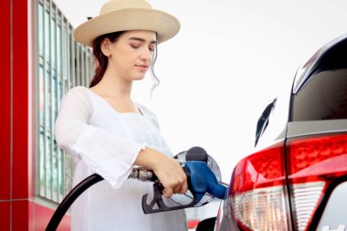 Portrait of happy smiling customer woman holding fuel petrol pump nozzle against for filling up her car, beautiful young lady traveler self refueling car with petrol at self-service gas station.