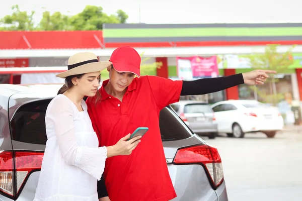 Beautiful woman traveler using mobile phone navigation while asking gas station attendant staff for finding right direction, cute female tourist getting lost and confusing in the city, asking for help.