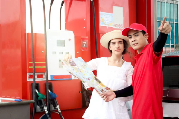 Beautiful woman traveler holding touristic map while asking gas station attendant staff for finding right direction, cute female tourist getting lost and confusing in the city, asking for help.