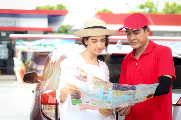 Beautiful woman traveler holding touristic map while asking gas station attendant staff for finding right direction, cute female tourist getting lost and confusing in the city, asking for help.