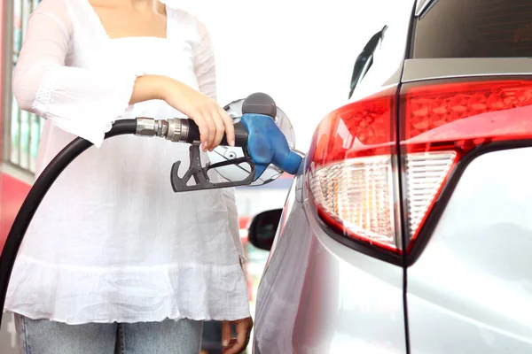 Blue fuel petrol pump nozzle against refueling auto car with petrol with female traveler holding touristic map and waiting as blurred background at gas station, customer woman self-refueling car.