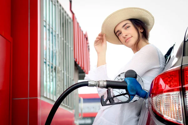 Blue fuel petrol pump nozzle against refueling auto car with petrol with beautiful female traveler waiting as blurred background at gas station, customer woman self-refueling car.