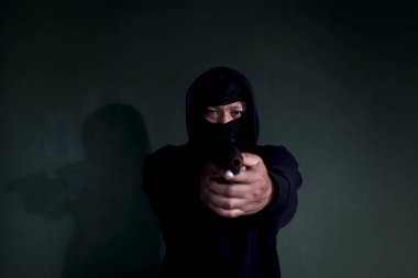 Siyah kapüşonlu bir suçlu, silah tutan bir kurban, maske hırsızı elinde silah, suç işlemek ve soygun yapmak için..