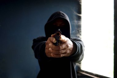 Siyah kapüşonlu bir suçlu, elinde silah tutan bir kurban, elinde silahı olan bir hırsız terk edilmiş bir binada suç işlemek için.