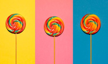 Sarı, pembe, mavi arkaplanda üç parlak renkli lolipop.