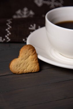 Kurabiyeler beyaz bir fincan tabağın ve kahverengi ahşap arka plan dikey bir fotoğrafın üzerinde bir fincan sade kahvenin yanına yakın plan şeklinde.