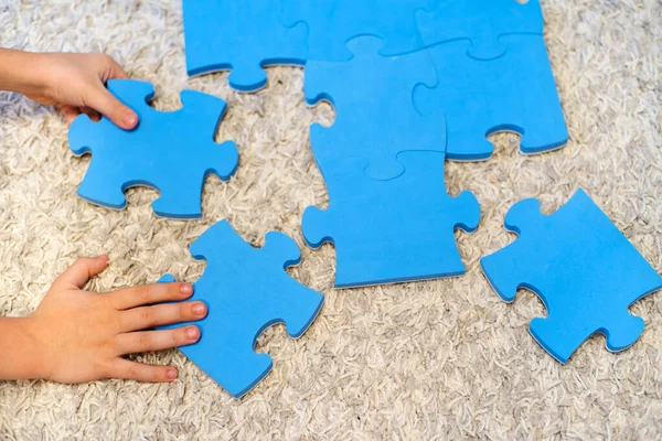 Çocuğun elleri halıya büyük bulmacalar koydu. Zeka ve mantık geliştiren çocuklar için oyunlar. Resimsiz detaylar. Tanınmayacak halde.