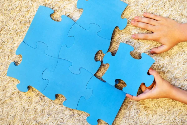 The child's hands collect puzzles on the carpet covered floor. There is no image. Template for the designer