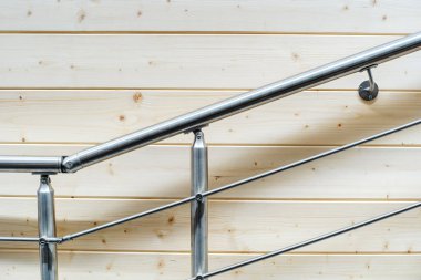 Stainless steel railing on a wooden wall background. Fragment of chrome-plated devices for safe stair climbing. Copy space