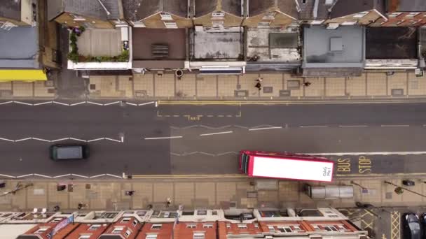 Drone seguindo um ônibus vermelho de dois andares que se afastou de uma parada de ônibus. — Vídeo de Stock