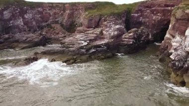 Dalgalar bir drondan görüldüğü gibi kayalık bir kıyıya çarpıyor..