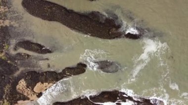 Deniz kıyısındaki büyük taşların üzerinden bir dron görüntüsü.