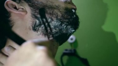 Sakal şekillendirme sürecini tehlikeli bir bıçakla filme almak. Arkaplan bulanık ve yeşil.