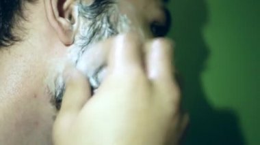 Bir adam sakalına yoğun bir şekilde tıraş köpüğü sürer. Koyu renk ve kalın sakallı yakışıklı bir adam. Planı kapat.