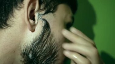 Genç gölgeli bir adam sakalını düz bir jiletle tıraş ediyor. Yakından bakınca, köpüklü kalın bir sakal görüyorum..