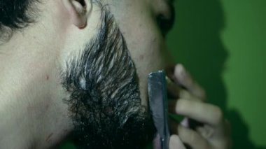 Sakalını ustura ile dikkatlice kesen genç bir adamın fotoğrafı. Düz bir usturayla traş olurken çekilmiş interaktif ev yapımı görüntüler..