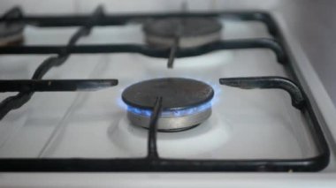 Çerçevede, bir adam gaz sobasını kibritle yakıyor. Arka planda siyah ocaklı temiz beyaz bir soba var..