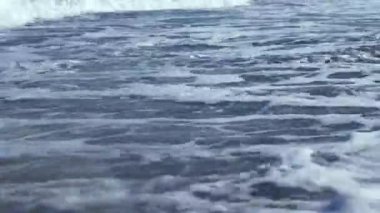 Bir bardak köpüklü deniz köpüğü. Dalgalar sürekli kıyıya vurur ve yüzeyde beyaz desenler oluşturur..