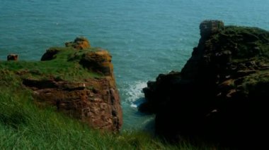 Önünde kayalık bir kıyı bulunan mavi Kuzey Denizi manzarası. İskoçya 'da Mayıs ayı başlarında yeşil kıyıları olan güzel kayalık kıyılar.