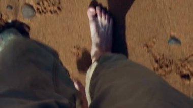 Kumlu bir plajda kaldırım taşlarıyla yürüyen birinin bacakları. Resim, Doğu İskoçya 'daki Kuzey Denizi kıyısı..