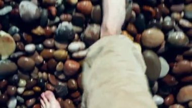 Kuzey Denizi kıyısında kum ve çakıl taşlarıyla yürüyen bir adamın bacakları. Güzel bir sahilden evrensel görüntüler.