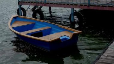 İskelenin yakınındaki dalgalarda sallanan küçük bir zevk teknesi. Gri köylü modern mavi tekne.