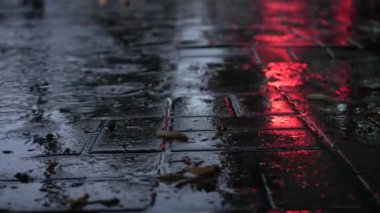 Gri bir günde su birikintileriyle dolup taşan fayanslardan yapılmış yürüyüş yolu. Damlalar yansımayı görebileceğiniz su birikintilerine vurur..