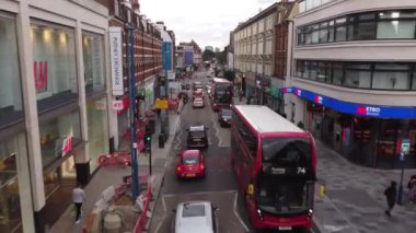 A quick drone footage of one of the small but busy streets in Putney, London. In the frame are beautiful small English houses and a street with many pedestrians, cars and shops.