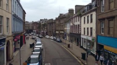 İskoçya 'nın küçük bir kasabasındaki işlek küçük bir cadde boyunca insansız hava aracının uçuşu. Arabalar yavaş hareket eder..