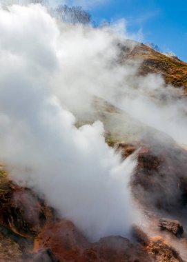 Volkanik aktivite bölgesinde gayzerden kaynar su ve buhar fışkırır. Kamçatka 'daki gayzerler vadisinde dağ yamacının ve mavi yay gökyüzünün arka planına karşı gayzer patlaması.