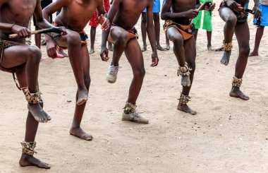 Halk kumda dans ediyor. Kumlu yüzeyde dans eden Afrikalıların ayakları. Ulusal dans gösterisi sırasında geleneksel süs eşliğinde beş çift çıplak bacak.. 