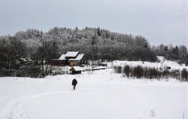 Silahlı bir adamın silueti kardan geçerek eve doğru yürüyordu. Avcı bulutlu kış gününde avdan döner..