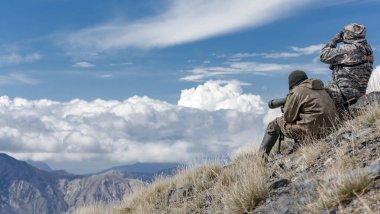 Hunters in the mountains are searching for cautious animals with binoculars and telescope. Hunters in the high mountains are searching for animals using optical devices. 