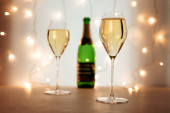 Dvě sklenice šampaňského nebo šumivého vína ve vánoční nebo novoroční atmosféře, láhev v pozadí, bokeh světla