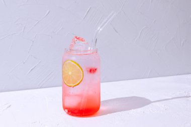 Gin and tonic cocktail with raspbery syrup in a highball glass with ice cubes and lime.