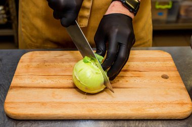 Aşçı mutfakta büyük bir bıçakla tahta bir tahtanın üzerinde şalgam kesiyor.