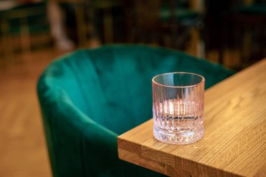 Kafedeki ahşap bir masanın kenarında pembe bir bardak su, yeşil bir sandalye. 