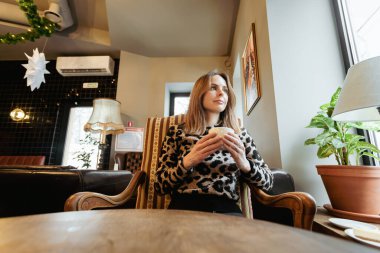 Pencerenin yanındaki kafede oturan beyaz bir kadın elinde bir fincan kahve ya da çay tutuyordu.