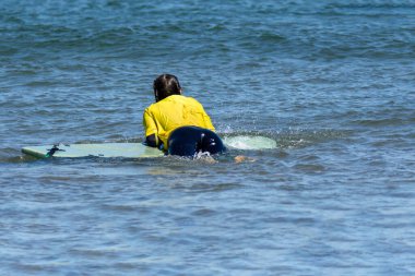 Back of a young caucasian woman relaxed on a surfboard in the sea