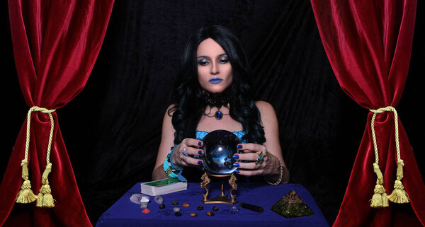 Экстрасенс с хрустальным мячом и карточками Таро с красными бархатными занавесками