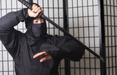 Ninja kostümü giyen ve elinde Ninja Silahları tutan Asyalı adam.