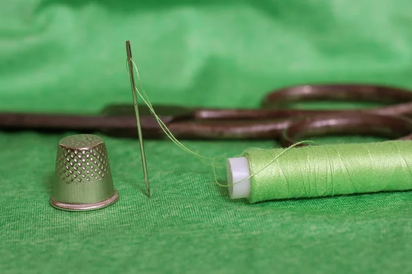 Катушка зеленой нити, наперсток и игла на зеленой ткани — стоковое фото