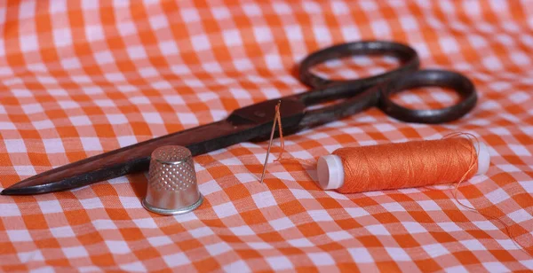 Orange und weiß karierter Stoff mit Fingerhut und Spule aus orangefarbenem Faden — Stockfoto
