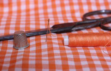 Portakal rengi ve beyaz kareli kumaş. Yüksük ve turuncu iplikli. Arkaplanda Klasik Makas