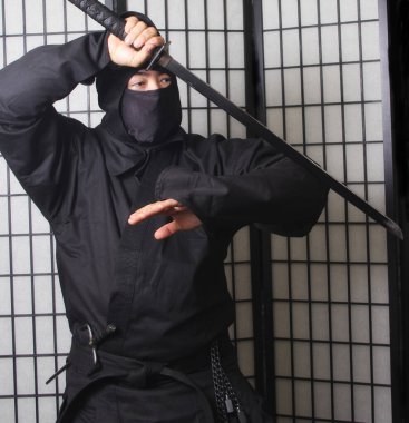 Ninja kostümü giyen ve elinde silah tutan Asyalı adam.
