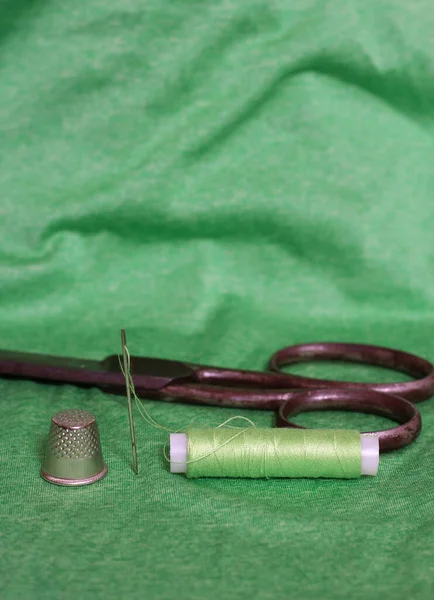 Spule aus grünem Faden, Fingerhut und Nadel auf grünem Stoff — Stockfoto